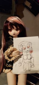 A photograph of a doll displaying a picture that she drew.